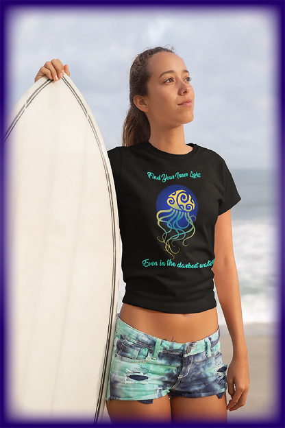 Young woman holding surfboard at beach wearing black t-shirt with jellyfish and inspirational quote